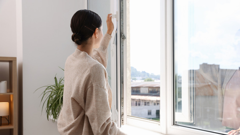 Woman opening large window with city view without any curtains or blinds