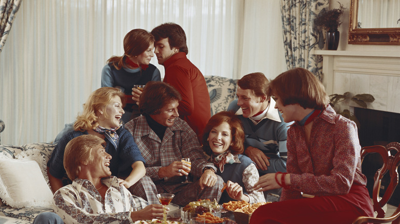 A group of people laughing and eating at a party in what appears to be the 1970s