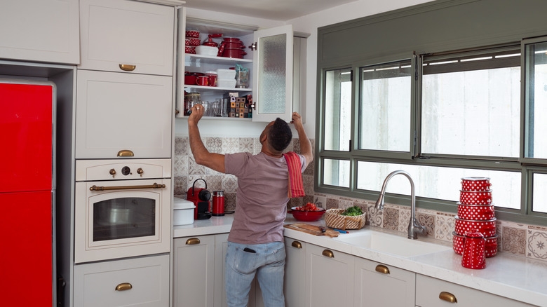 A man stands in front of a cabinet in a kitchen, looking inside.