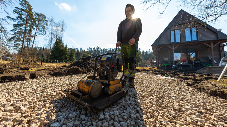 Worker using vibratory compactor to level driveway