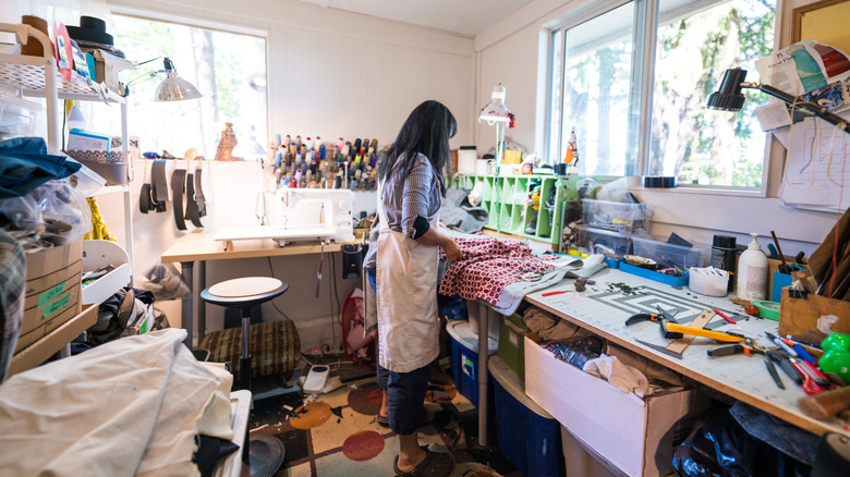 A woman stands in the middle of a messy craft room