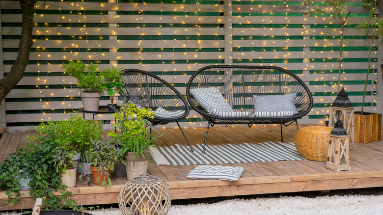 Cozy patio setup with lots of plants, cushions, and outdoor lanterns.