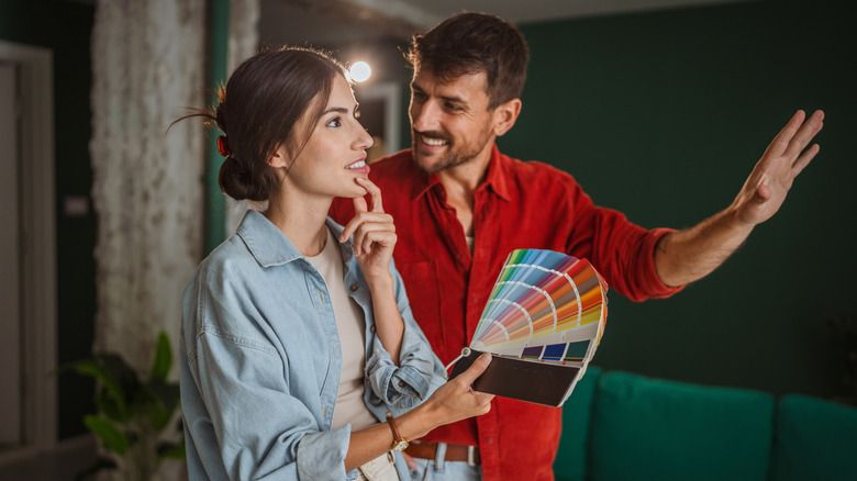 Two people look at a wall while holding paint swatches.