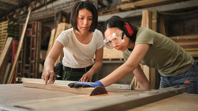 Two people use a saw to cut wood in a shop