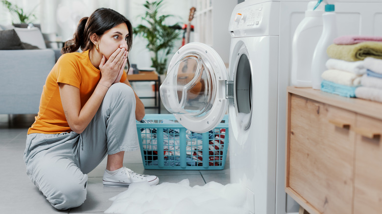 A worried woman looks at a broken washing machine