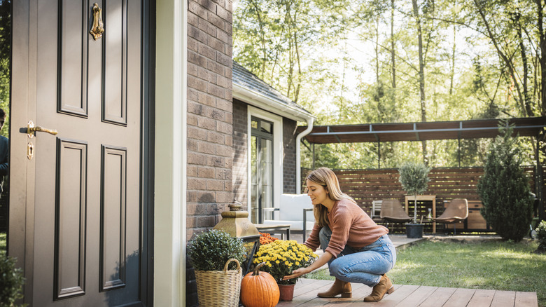 A woman kneels next to a potted plant in front of an old-fashioned black front door