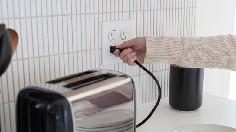 Plugging a toaster into an electrical outlet