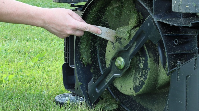 Person scraping underside of lawn mower deck with a scraper