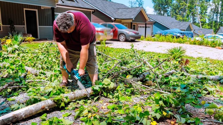 Man cutting branches with a chainsaw in front of his home