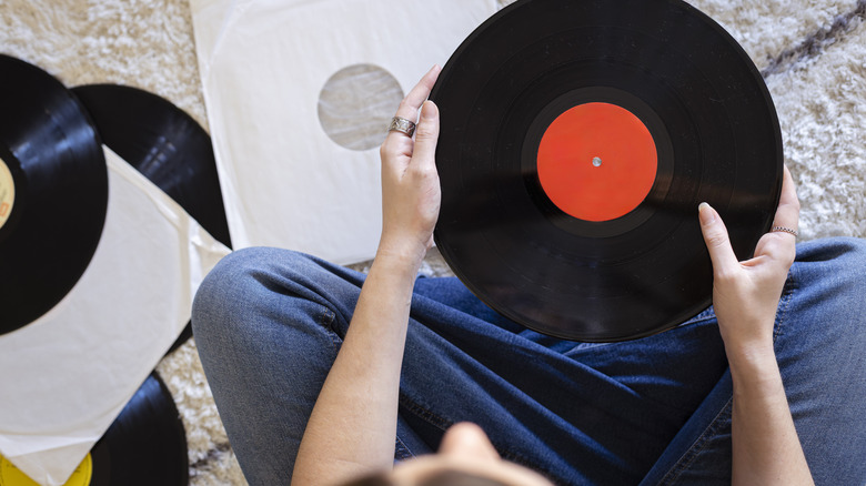 A woman holds a black and red vinyl record on a carpeted floor