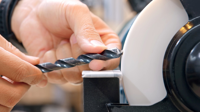 A person uses a bench grinder to sharpen drill bits