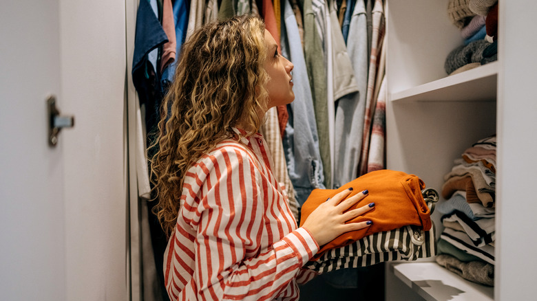 A woman puts clothing into an overflowing closet.
