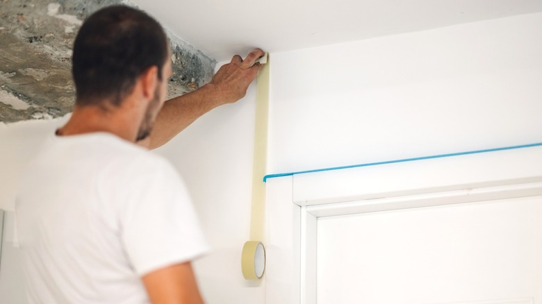 A man holding white painter's tape on a wall while blue painter's tape lines a door frame