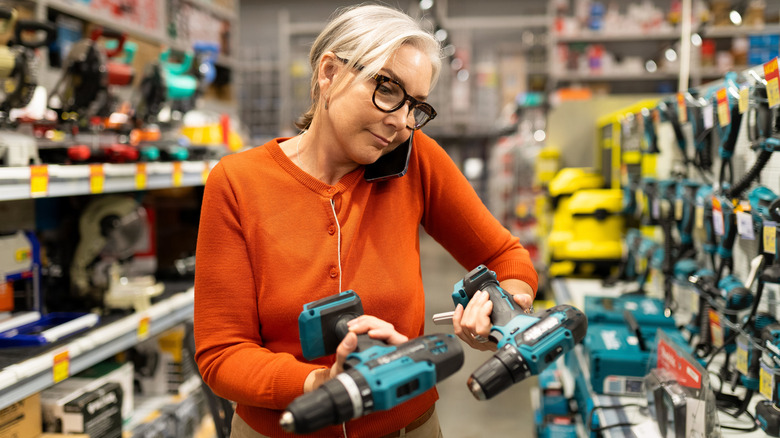 A woman examining two power tools in a store