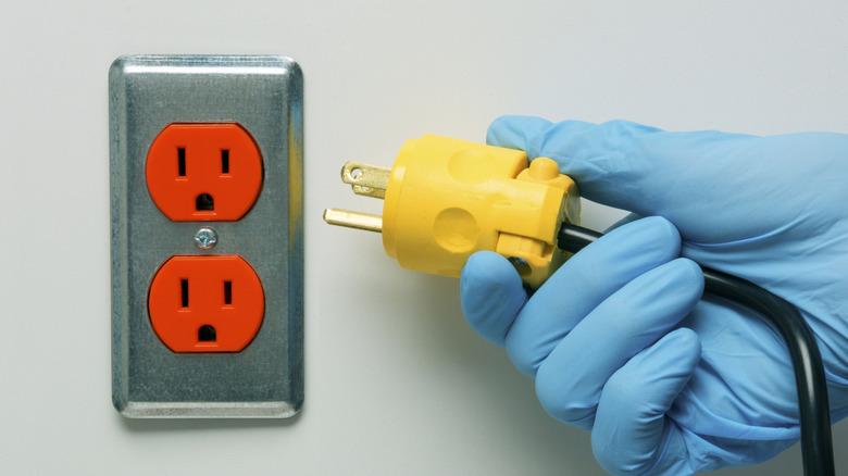 An orange electrical outlet with gloved hand holding plug
