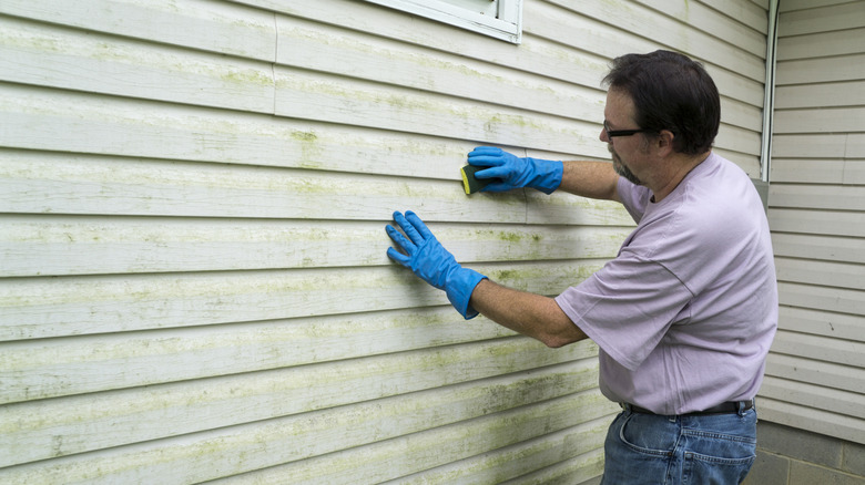 A man is scrubbing a dirty vinyl siding