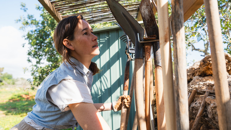 woman grabbing garden tools from storage