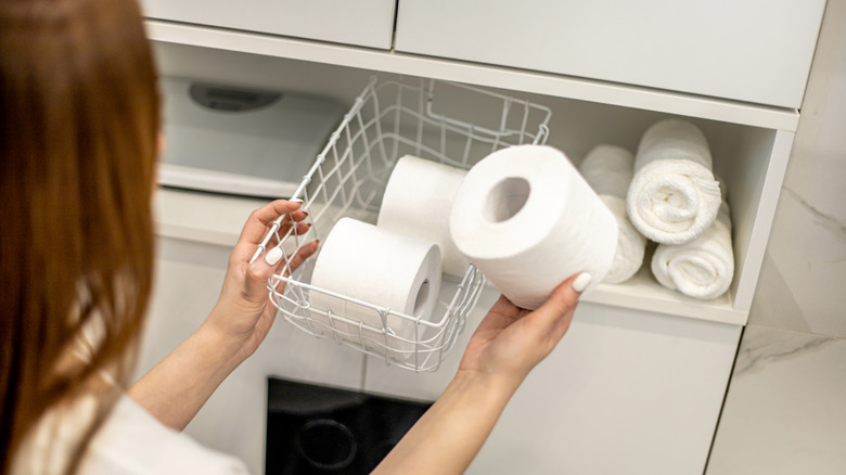 A person putting toilet paper into a wire basket