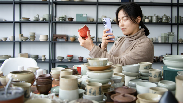A woman takes a photo of pottery in a thrift store
