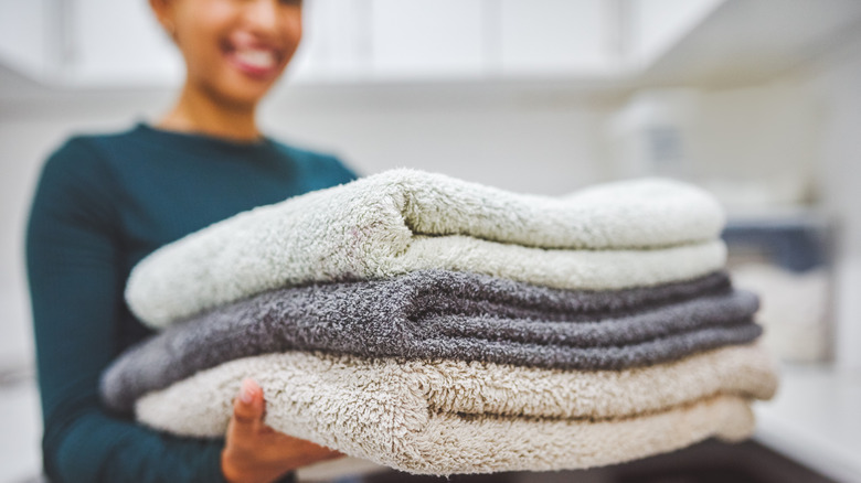 A woman smiles while holding a stack of bath towels