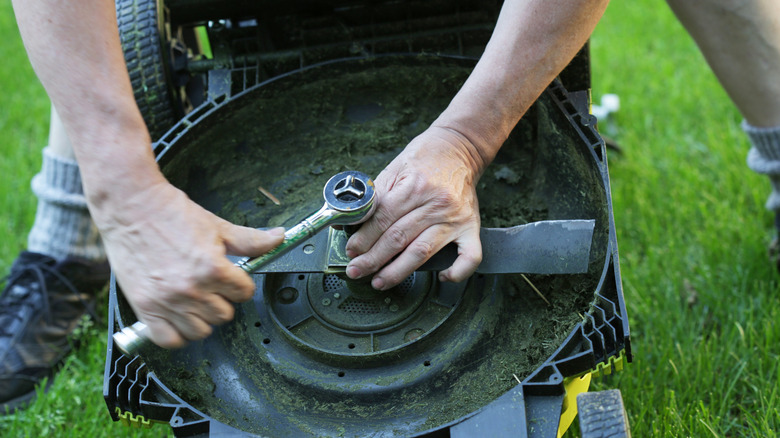 A person's hands removing a lawn mower blade