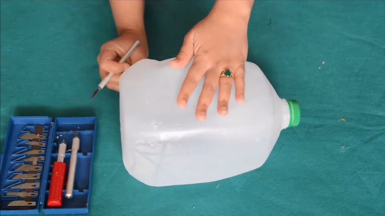 Person holding an empty milk carton on a work surface with cutting tools next to it