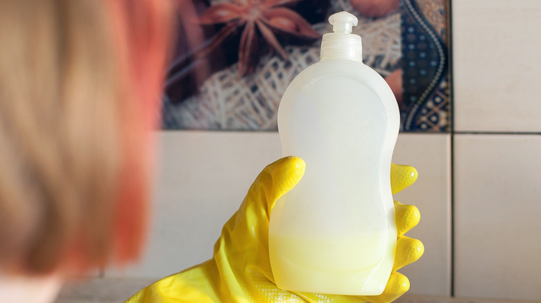A person holding a nearly empty bottle of dish soap
