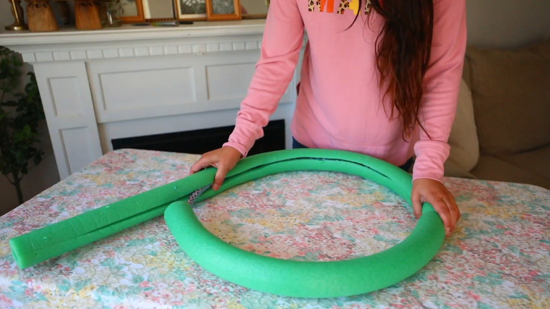 A woman folds a green pool noodle on a table