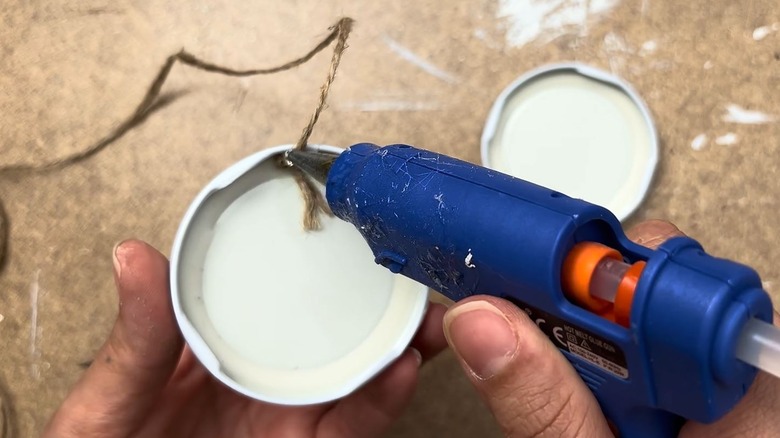 Woman using a glue gun to adhere a string to an old jar lid