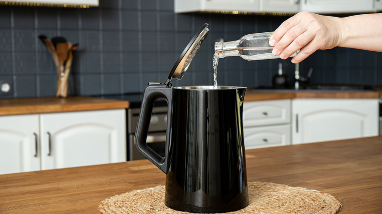 Person pouring distilled vinegar into electric kettle for descaling