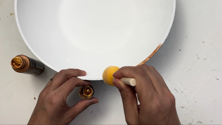 Woman dabbing bronze paint over a white frying pan