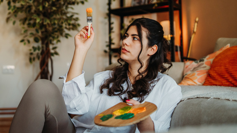 A woman holds a paintbrush and palette