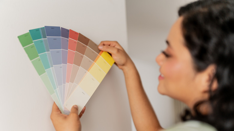 Woman looking at paint swatch card in front of plain wall