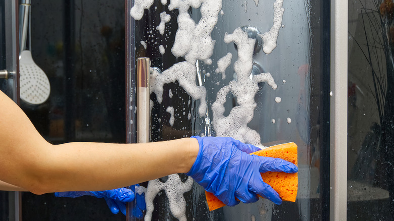 Woman cleaning glass shower door with sponge