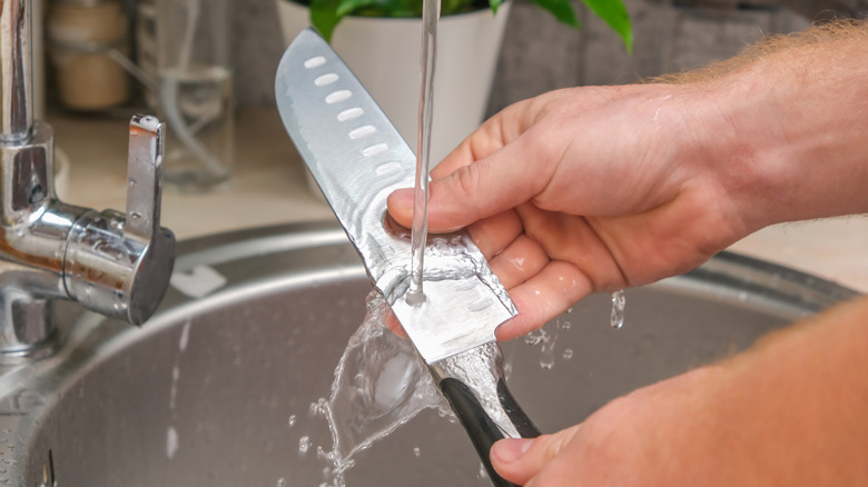 Hands washing a knife in the sink