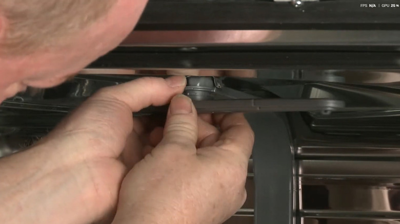 Hands installing a new upper wash arm in a Frigidaire dishwasher