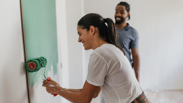 Two people using a roller to paint a wall green.
