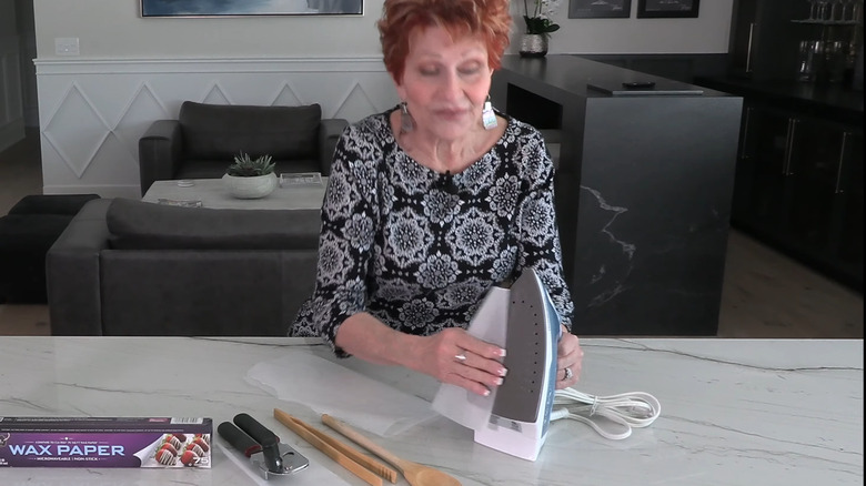 Woman rubbing wax paper on the plate of a clothes iron
