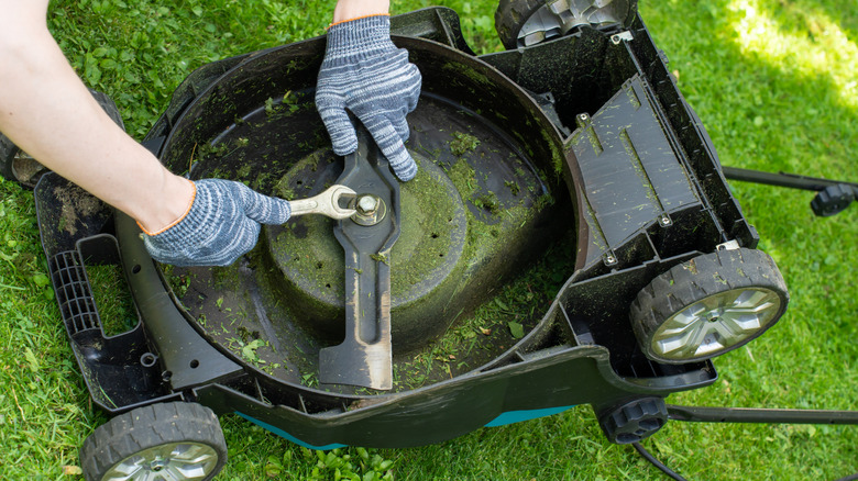 Gloved hands tightening the blade on a lawn mower