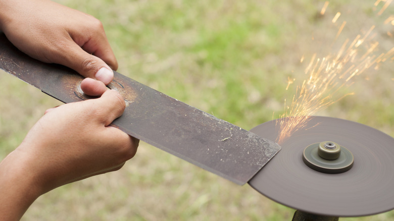 Hands are shown sharpening a lawn mower blade