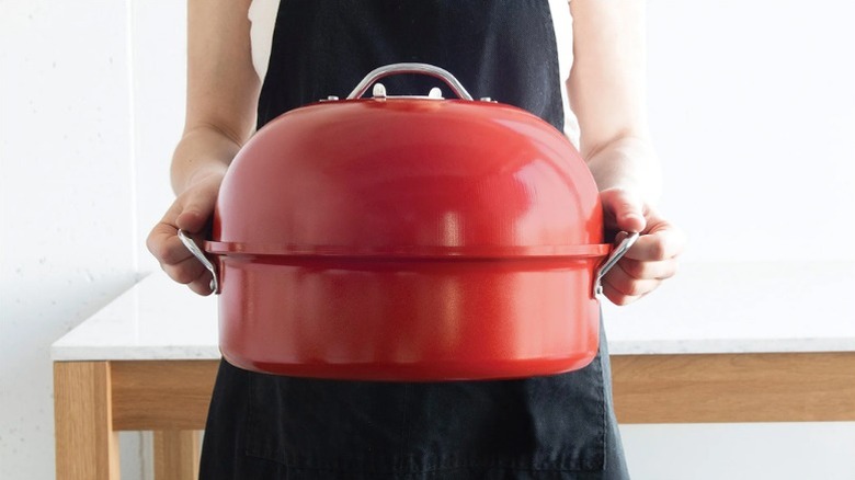 Person holding a red Nordic Ware kettle smoker