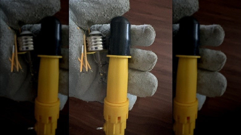 Gloved hand holding Bayco tool and broken bulb components