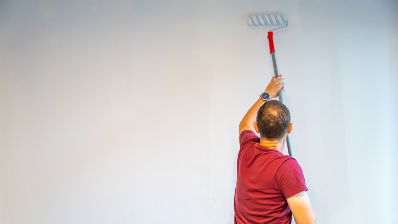 Man using an extended roller paint brush to paint a wall