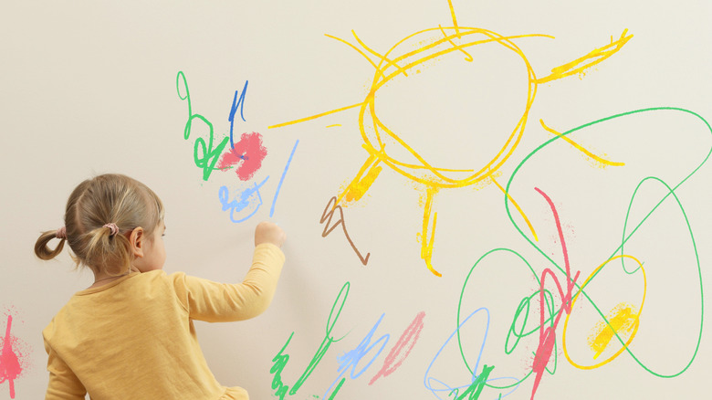 A child is drawing on a painted wall with crayons