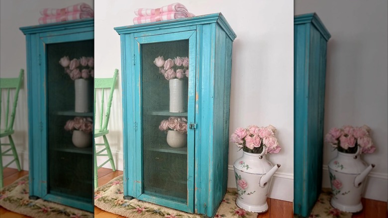 A vintage teal blue pie safe is decorated with pink faux flowers