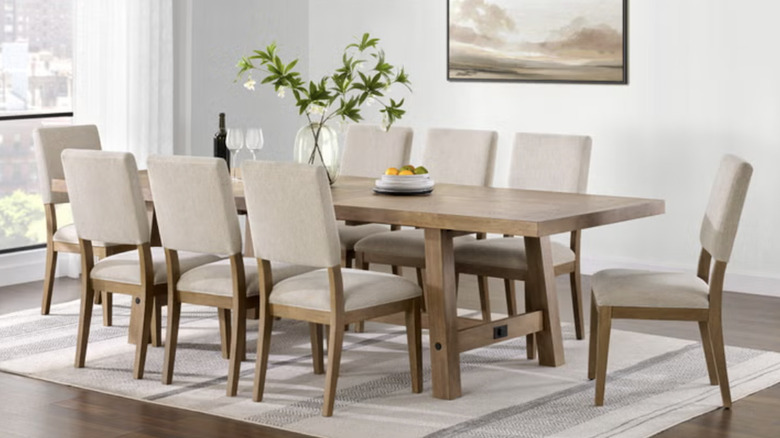 Pike & Main Graham Dining Table in tan under a rug and next to a window and white wall with a photo