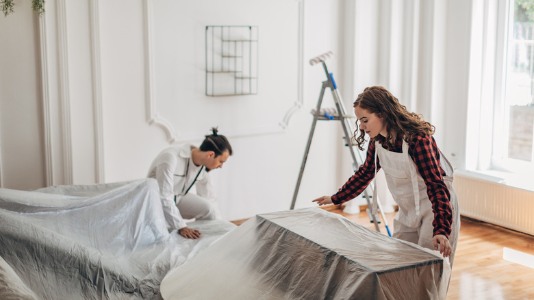 A couple is covering their furniture in plastic before painting a room