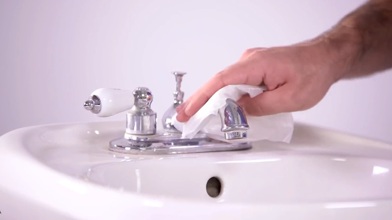 Rubbing wax paper on a bathroom faucet