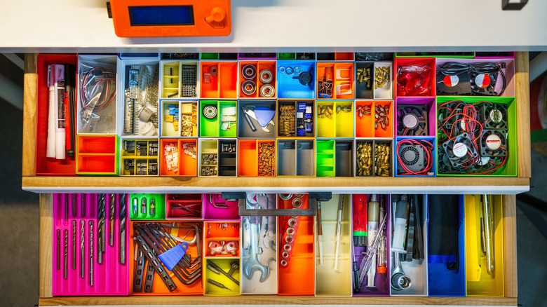 Small items are organized in colorfully painted printers trays inside a desk drawer