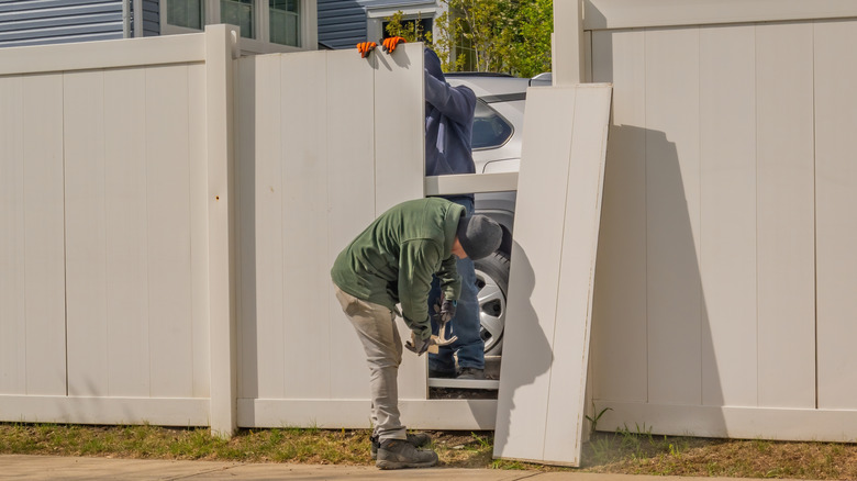 Contractors install an ivory vinyl fence panel